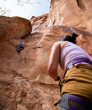 person belaying another person rock climbing in a canyon