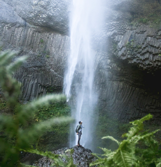 man sitting in the foreground of a waterfall