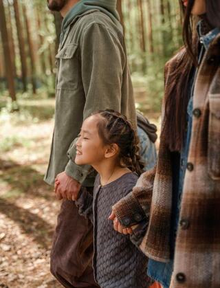 a young child smiling and holding hands with two adults in the woods